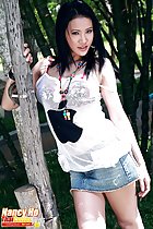 Standing against tree wearing white top in denim short skirt