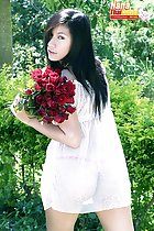 Looking over her shoulder long hair holding roses wearing white transparent dress in thong panties