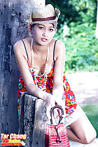 Leaning against tree stump wearing hat in summer dress