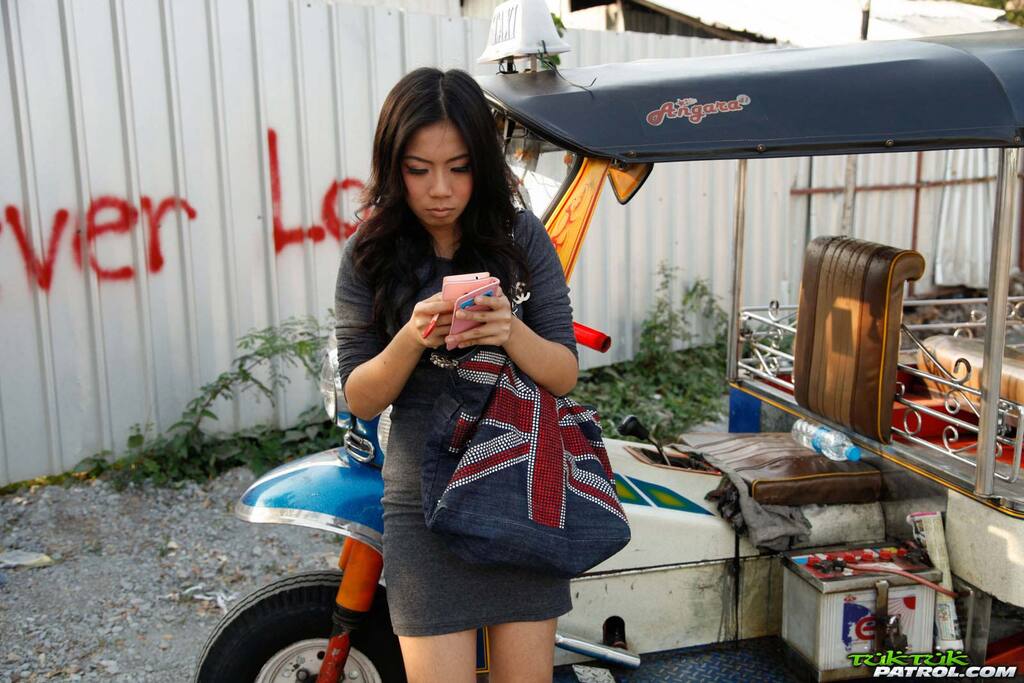 Standing beside tuktuk looking at her phone